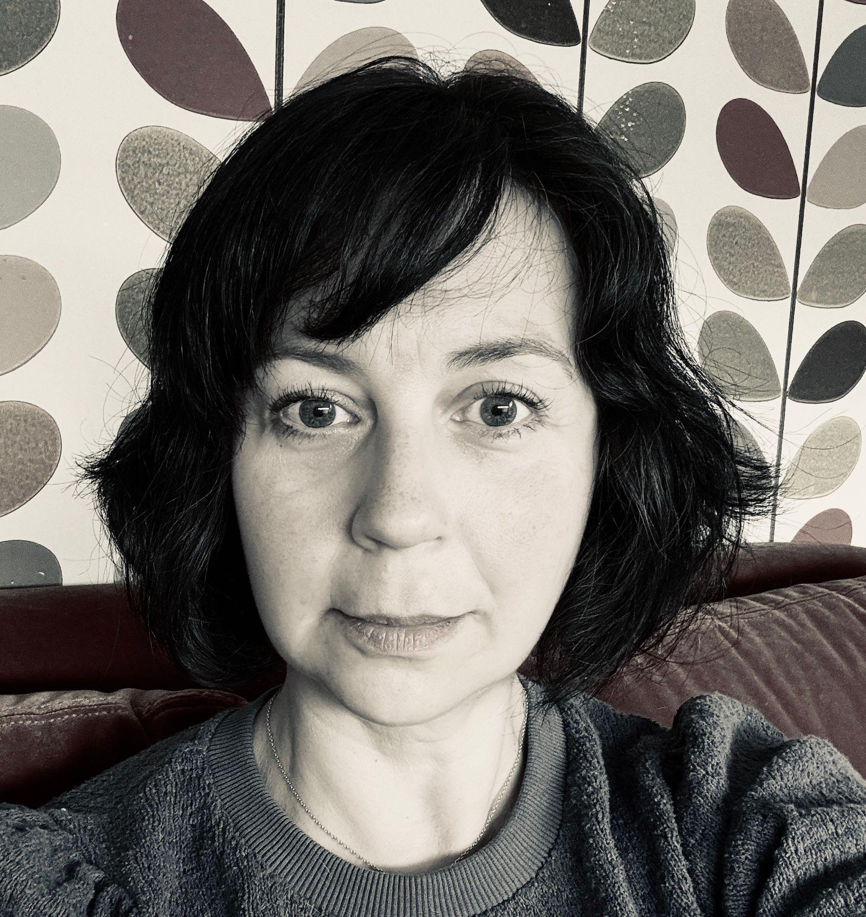 Black and white portrait of a woman with short dark hair, in front of a patterned wall.